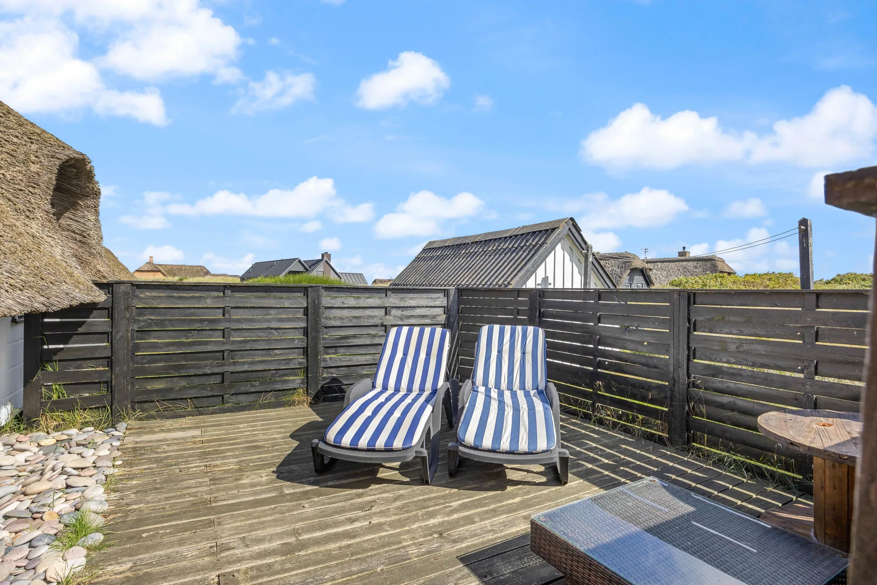 A wooden outdoor deck has two blue-and-white striped loungers beside dark fencing.