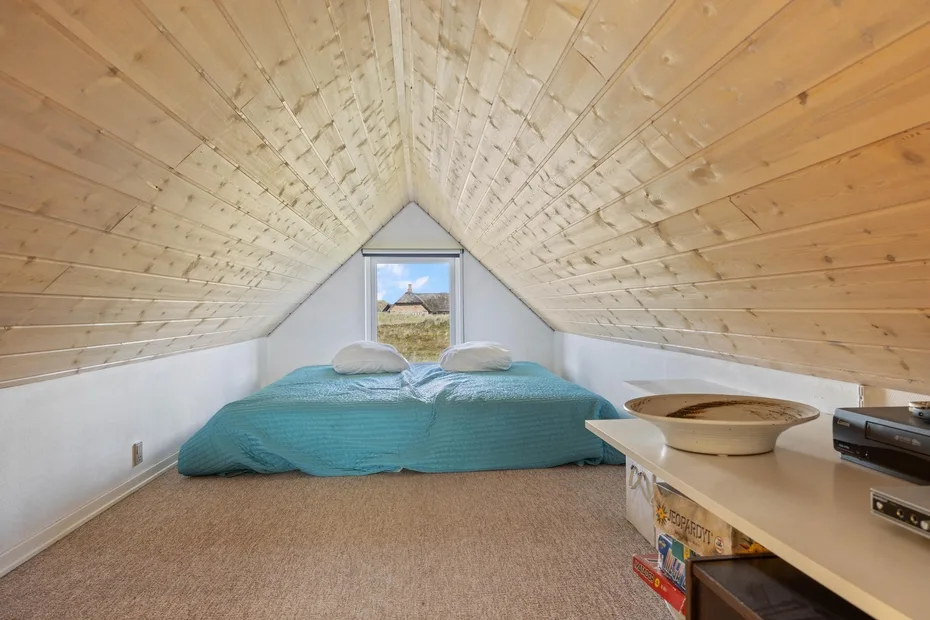 A bedroom with a low bed beneath a sloped wooden ceiling.