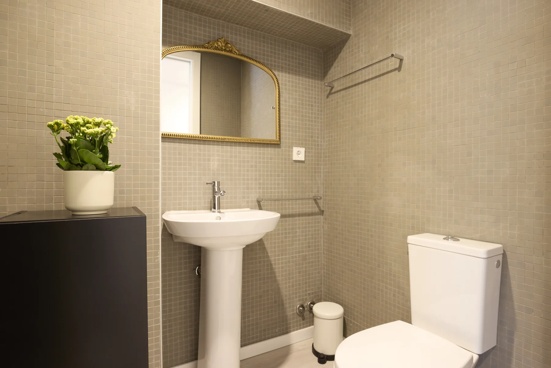 A tiled bathroom with a pedestal sink, mirror, and toilet.