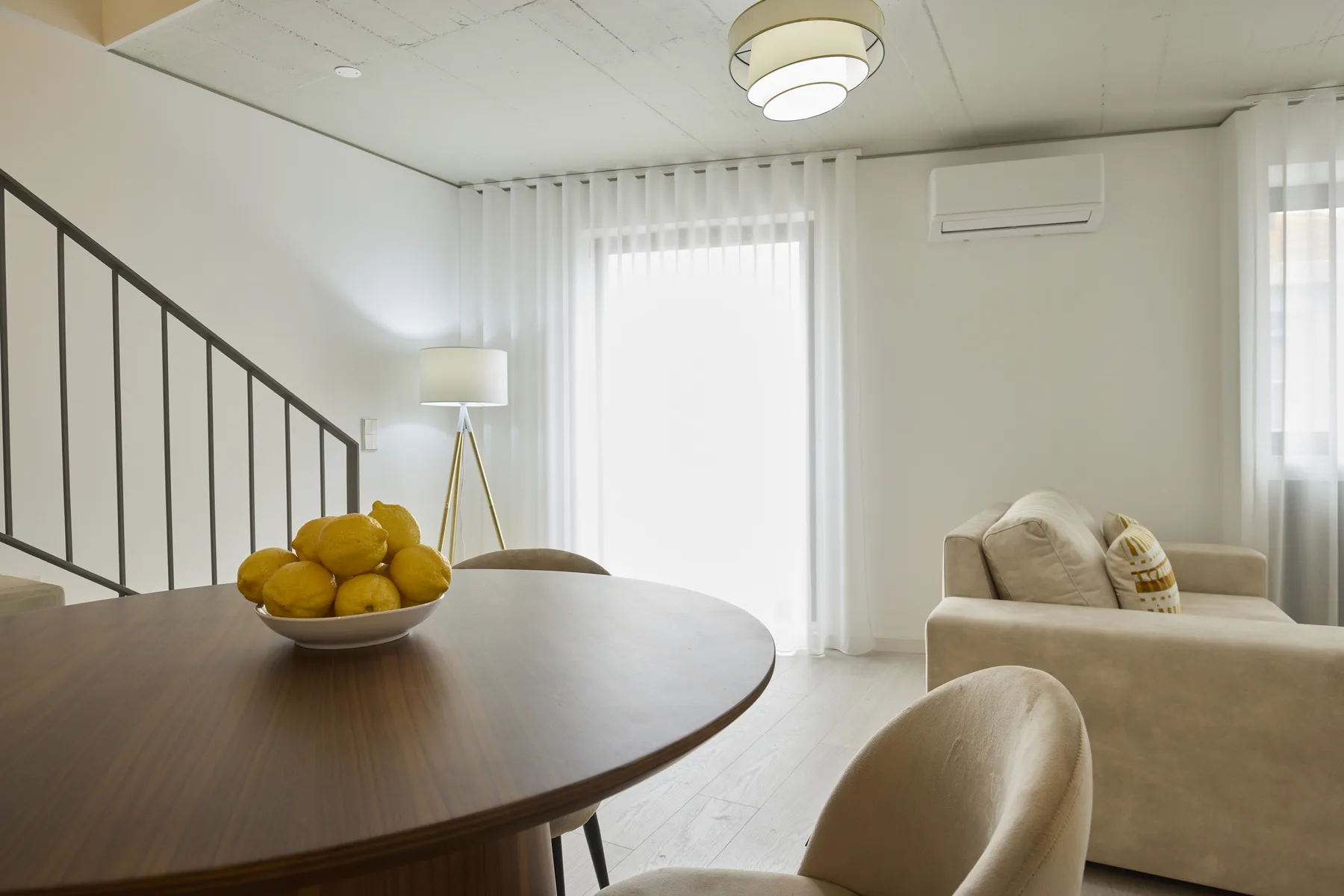 A bright living room with a dining table and seating beside tall windows.