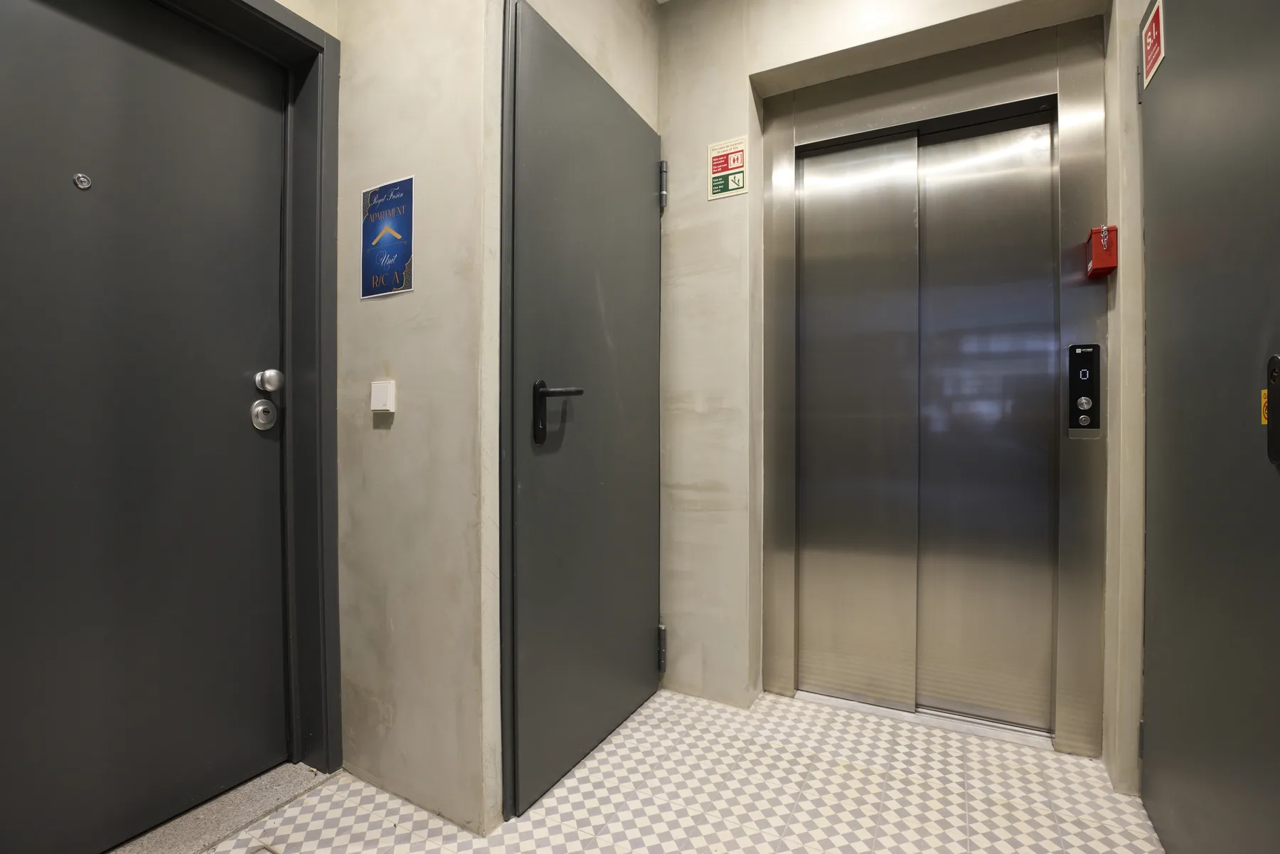 An elevator lobby with metal elevator doors and dark entry doors.