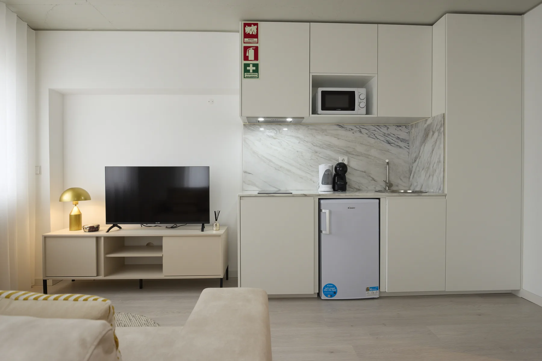 A living area with a television beside a compact kitchenette.