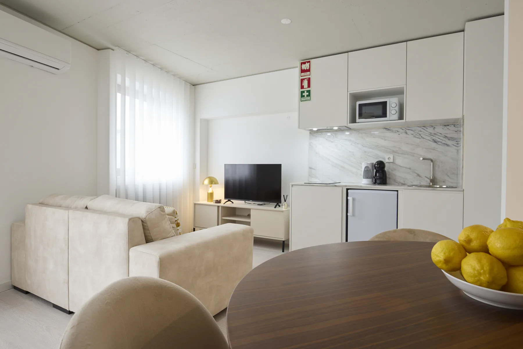 A bright living room with seating, a television, and a dining table beside a compact kitchen.
