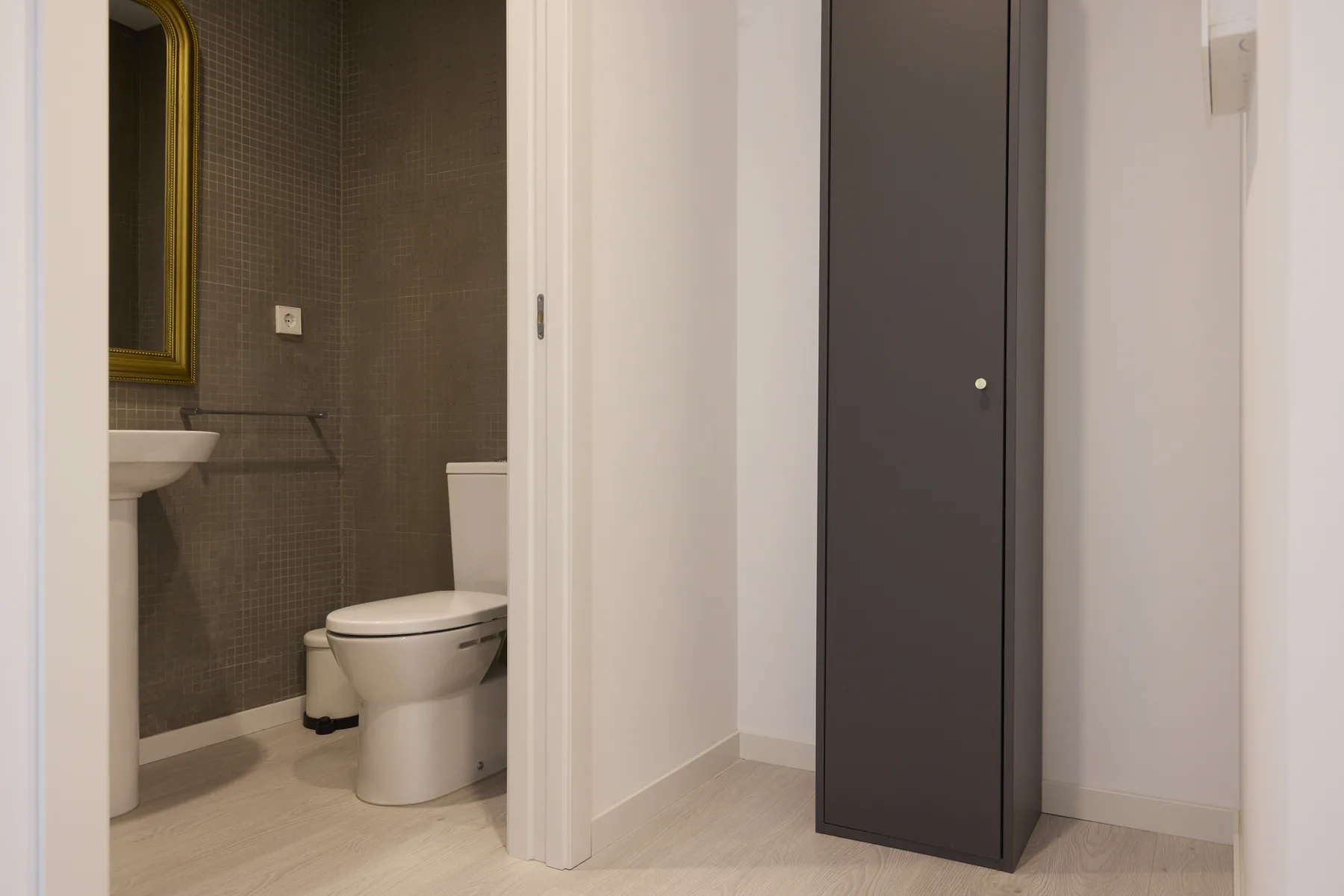 A bathroom with a sink and toilet is visible beside a dark door.