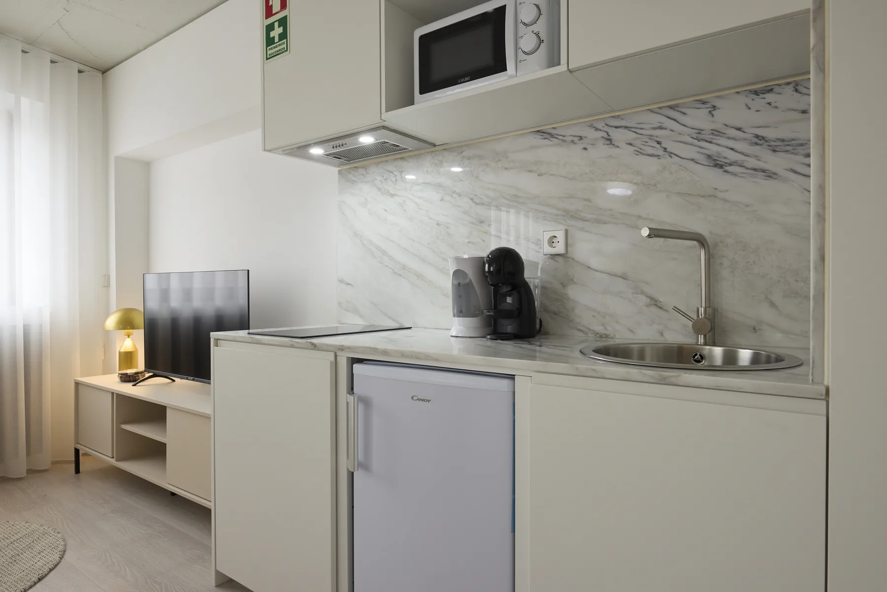 A compact kitchenette with a sink and coffee maker beside a curtained window.