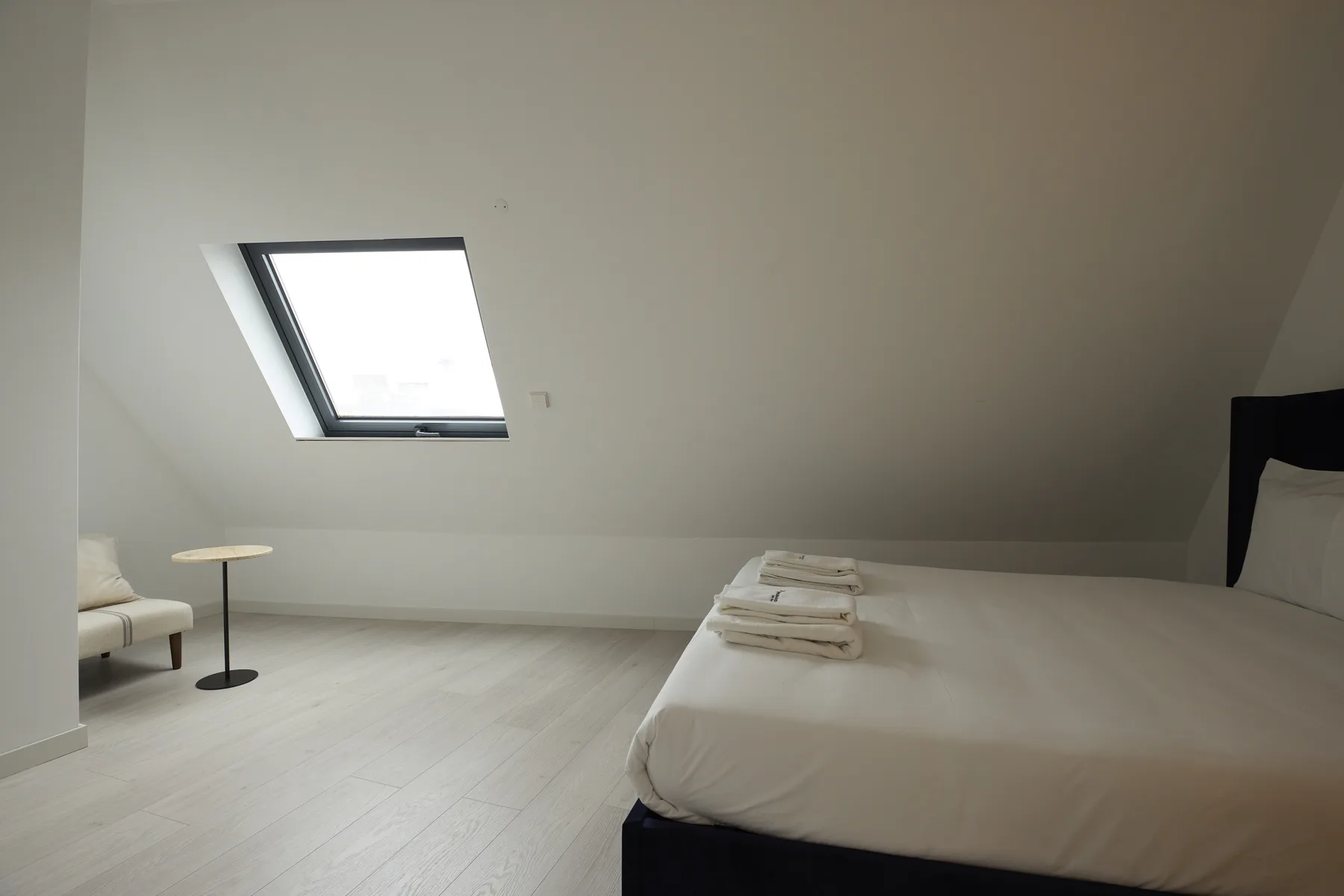 A bedroom with a bed, folded towels, and a skylight.
