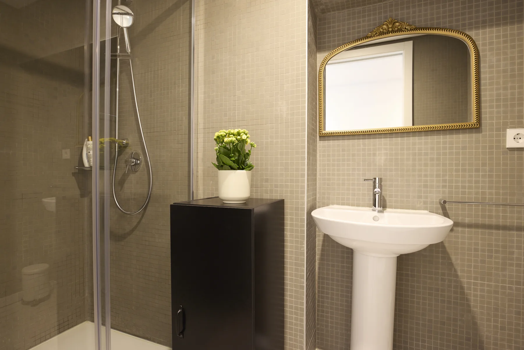 A tiled bathroom with a shower, pedestal sink, and mirror.
