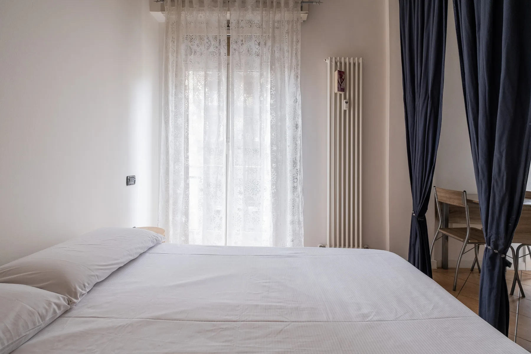 Un dormitorio con una cama junto a una ventana cubierta por cortinas translúcidas.