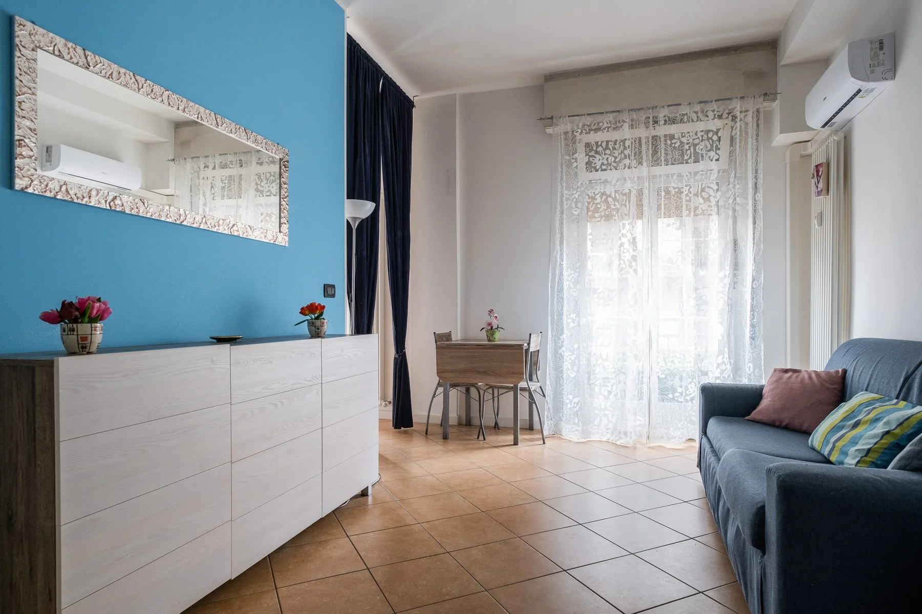 Una sala luminosa con un sofá azul junto a una ventana grande.