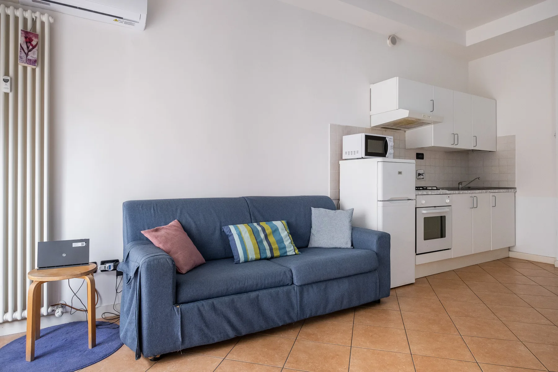 Una sala de estar con asientos azules junto a una cocina compacta.