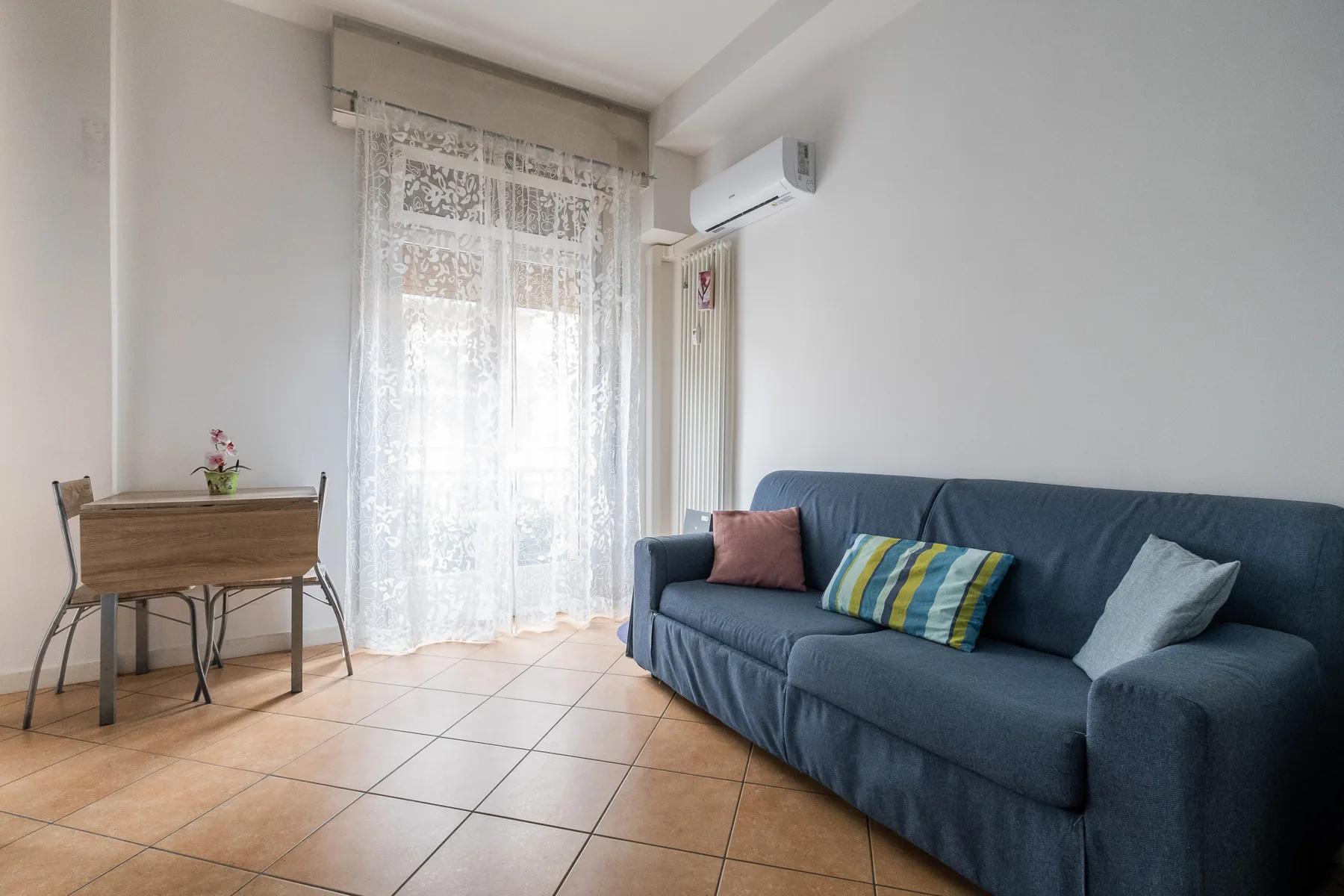 Una sala de estar con un sofá azul junto a una ventana luminosa.