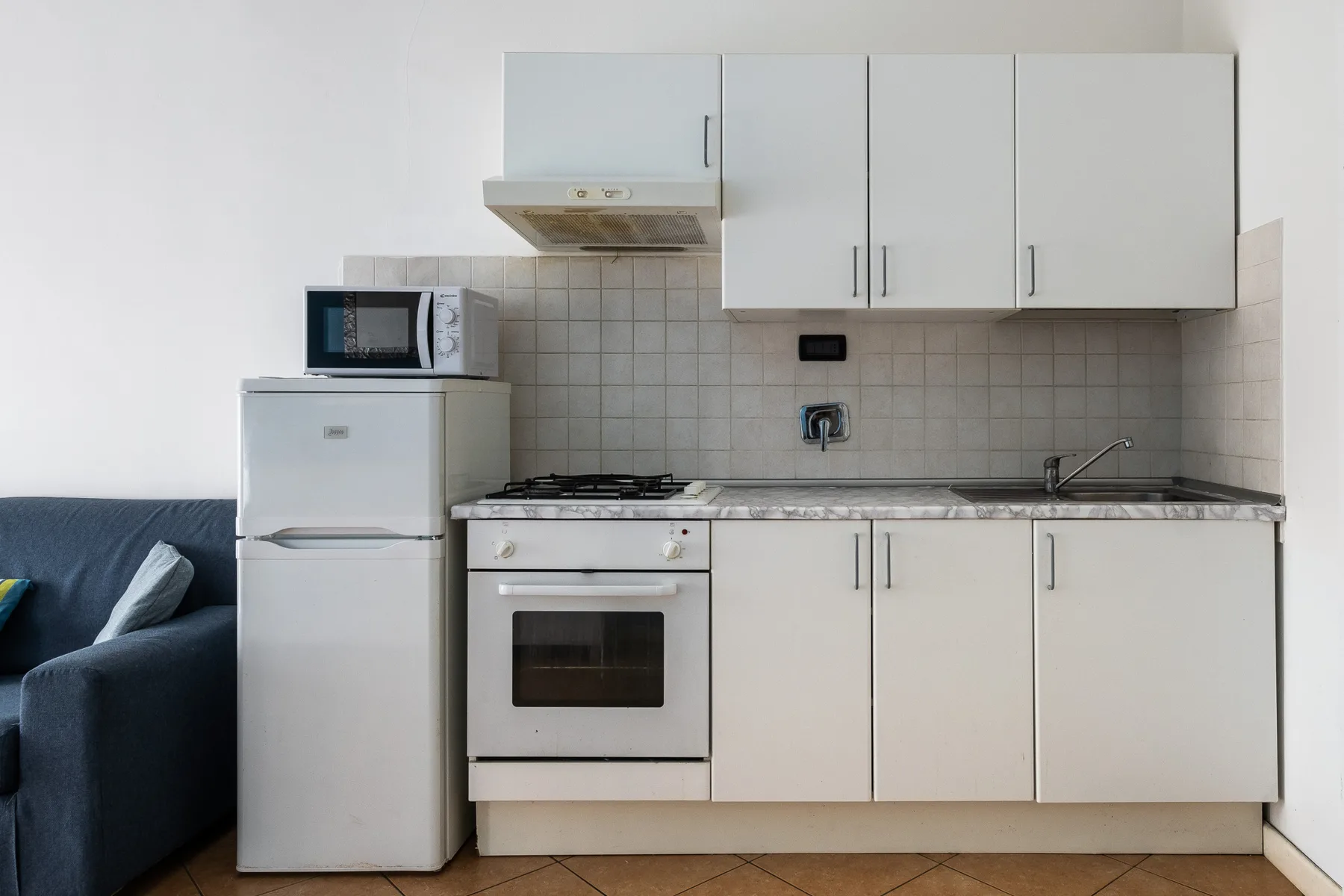 Una cocina compacta con gabinetes blancos, una estufa y un refrigerador.