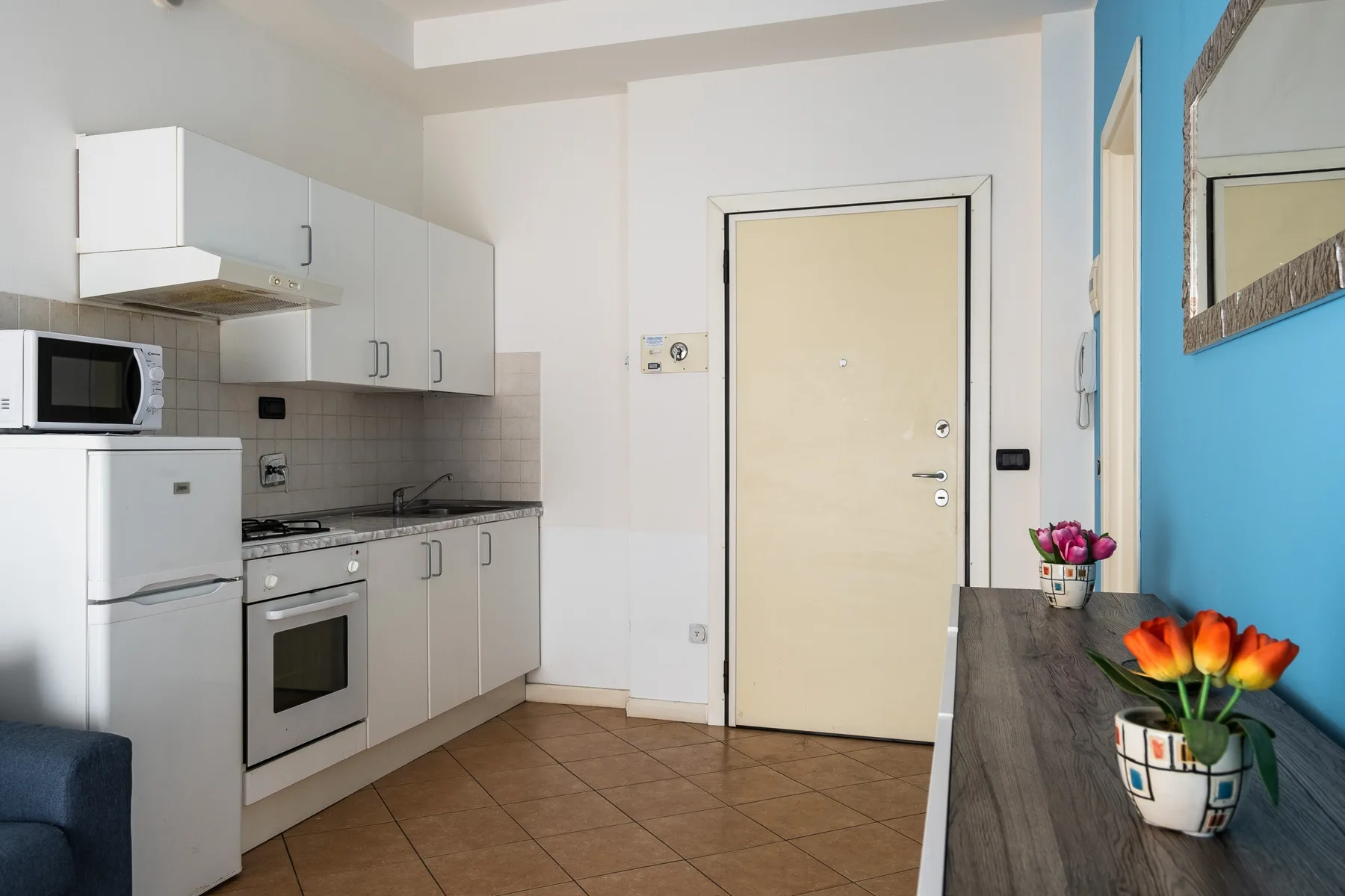 Una cocina compacta con armarios blancos, electrodomésticos y una encimera decorada con flores.
