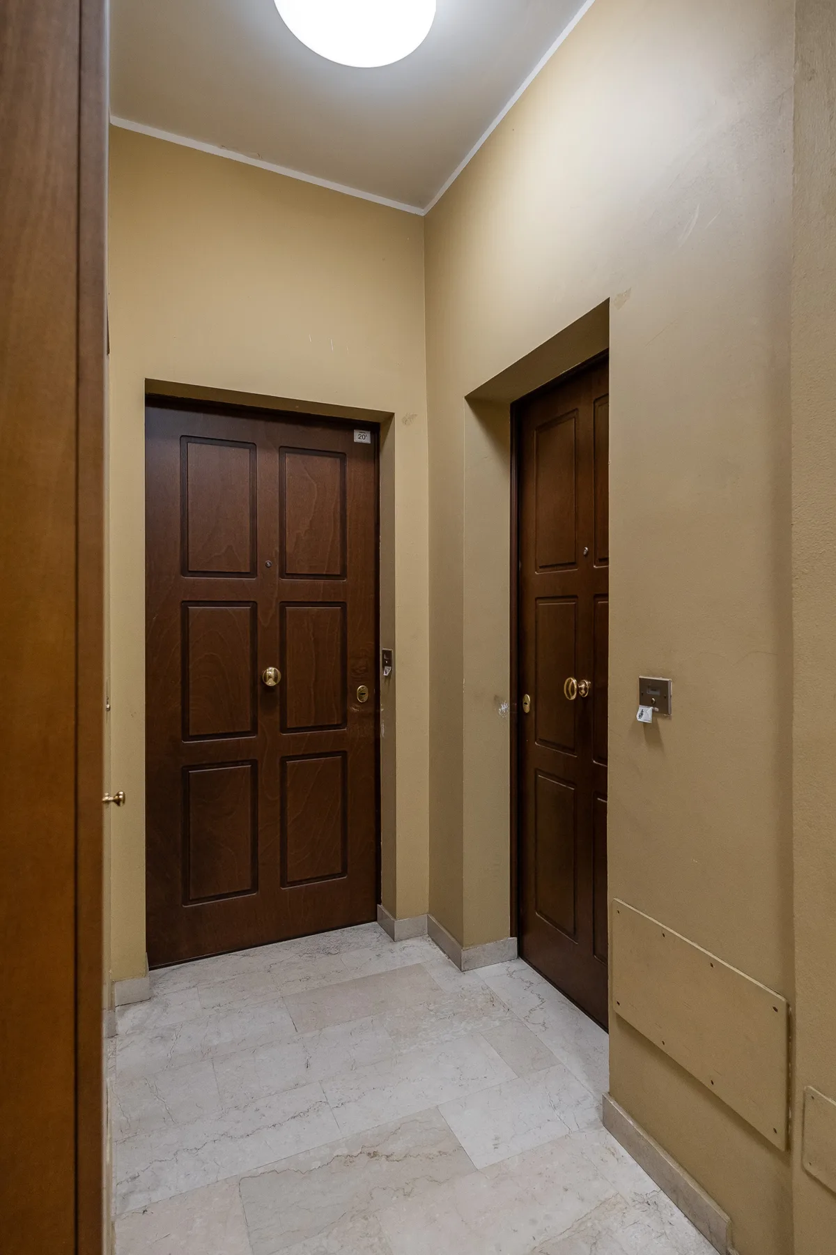 Un pasillo beige con dos puertas de madera oscura y suelo de baldosas claras.