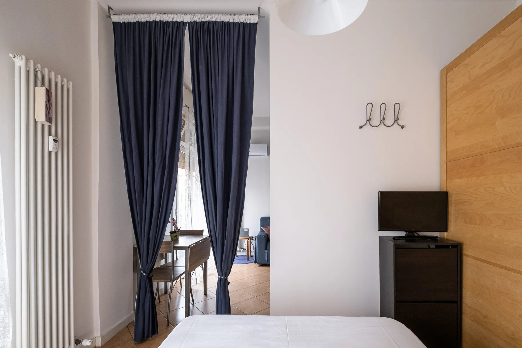 Un dormitorio con una cama, cortinas oscuras y un televisor sobre un mueble.
