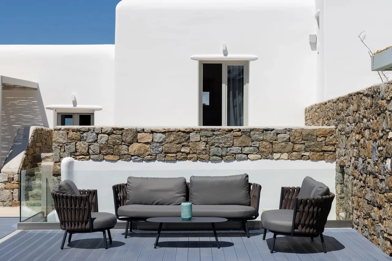 An outdoor seating area sits beside a stone wall and white buildings.
