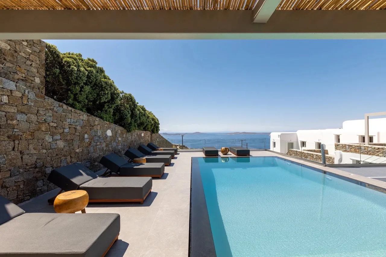 An outdoor swimming pool beside lounge seating, with the sea visible beyond.