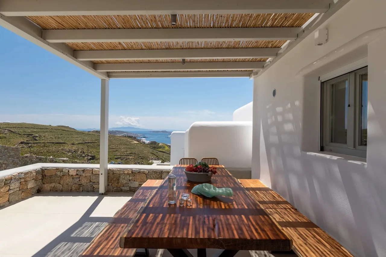 A covered outdoor dining terrace with a wooden table overlooking the sea.