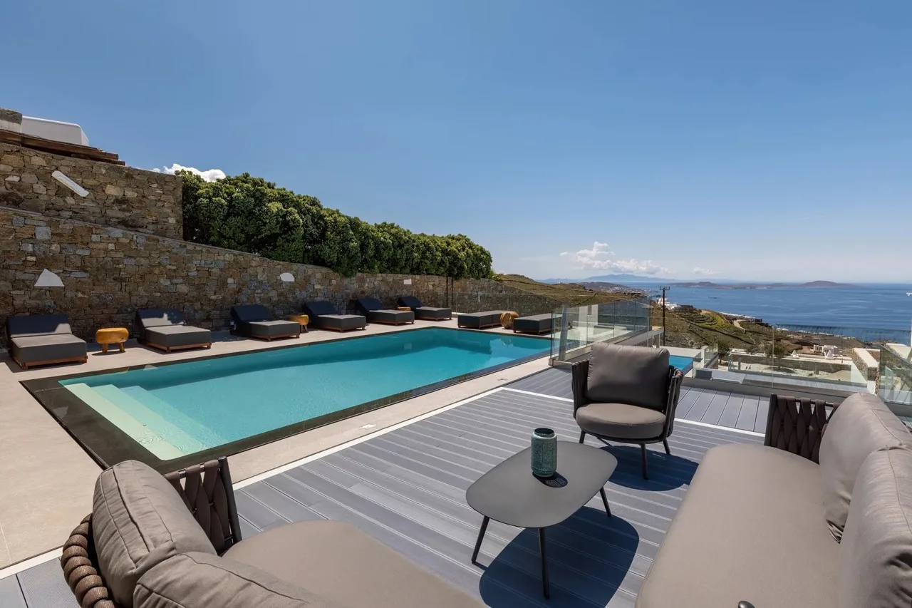 A swimming pool and outdoor seating overlook the sea beneath a clear sky.