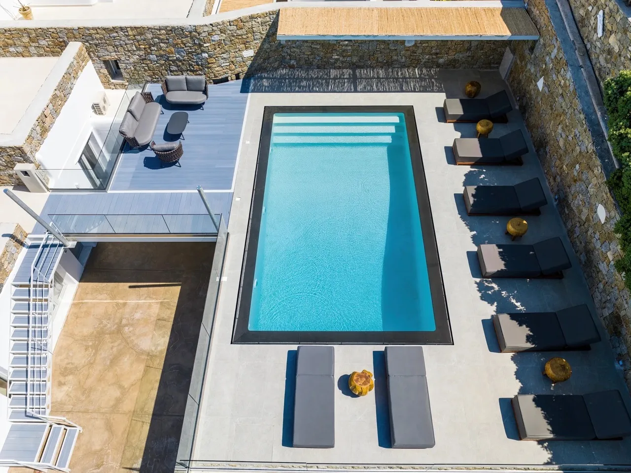 An outdoor swimming pool is surrounded by lounge seating on a paved deck.