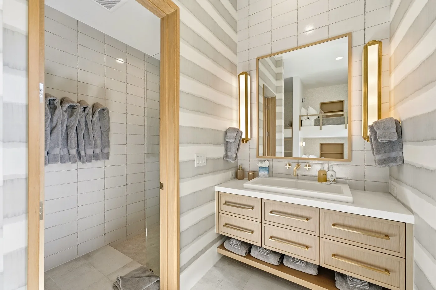 A bright bathroom with a tiled shower and a wide vanity beneath a mirror.