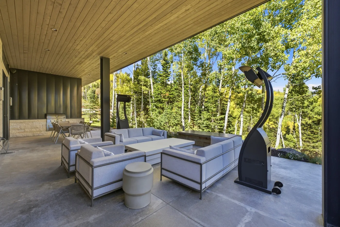 A covered outdoor lounge with cushioned seating overlooking leafy trees.