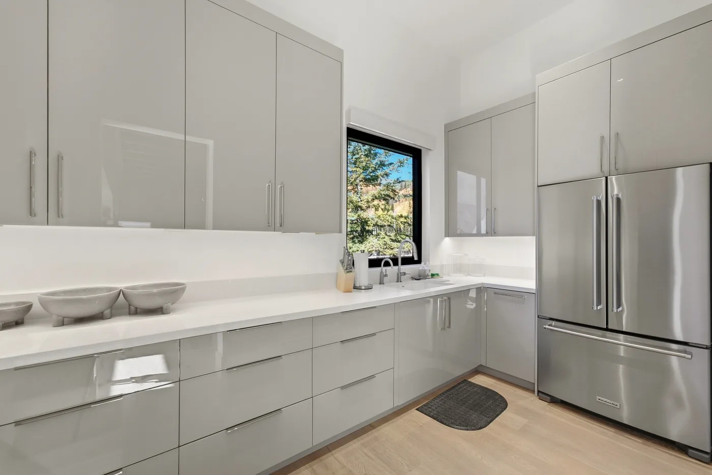 A bright modern kitchen with pale cabinets, a long counter, and a window.