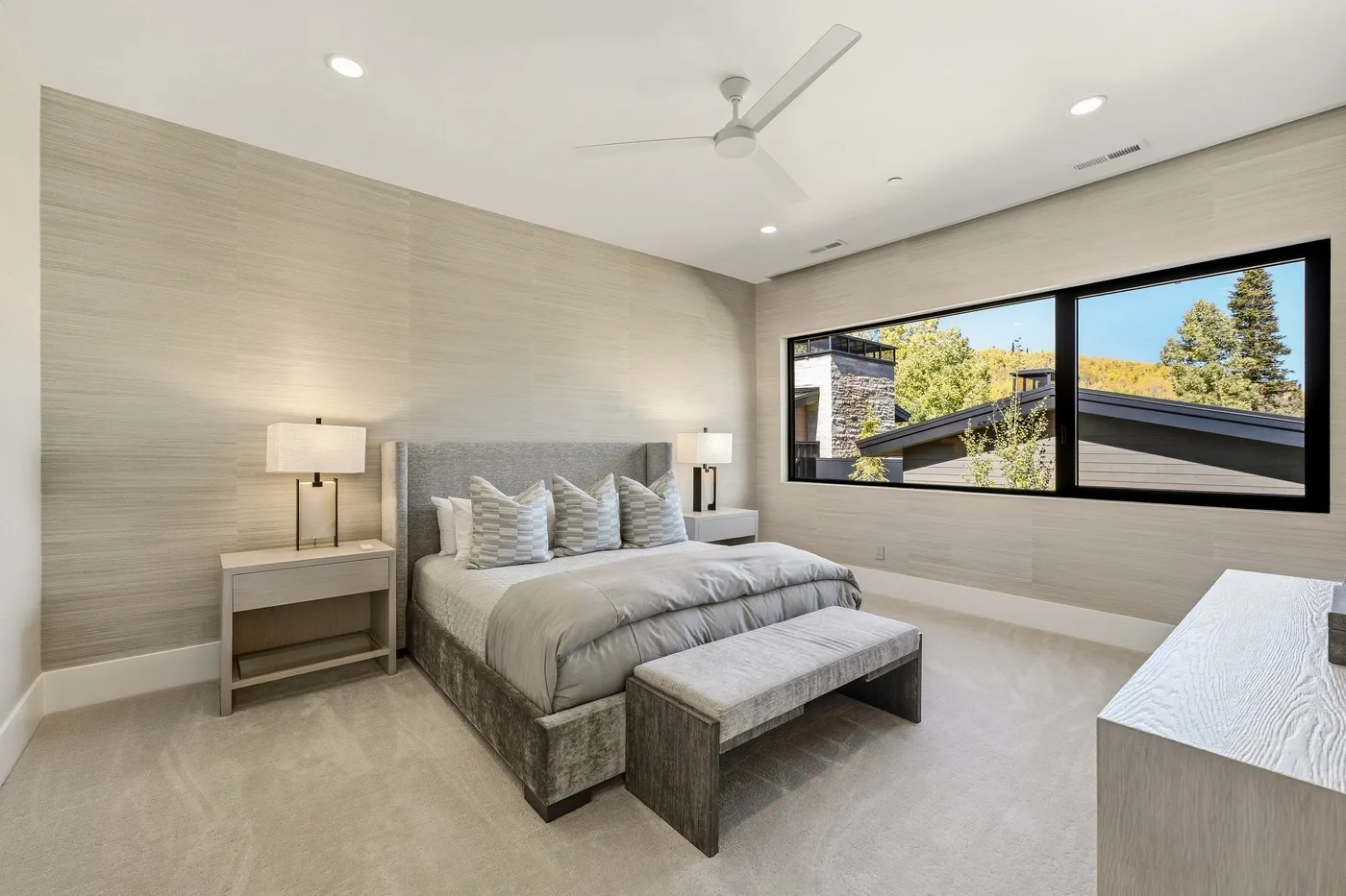 A bright bedroom with a neatly made bed and a wide window.
