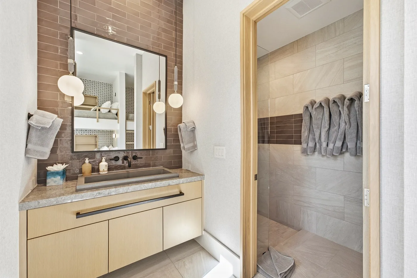 A bathroom vanity with a large mirror sits beside a tiled shower.