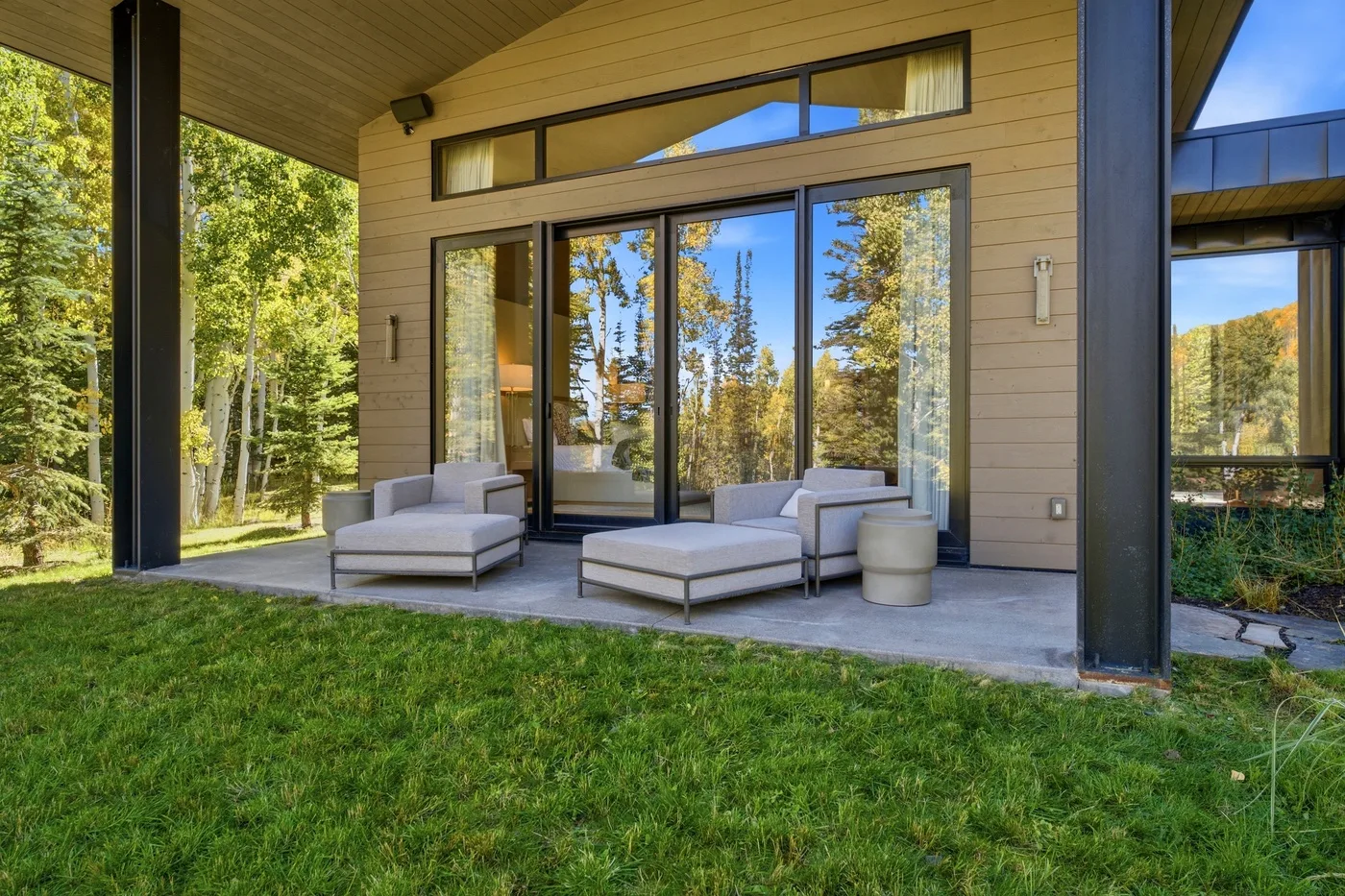A covered outdoor seating area beside large glass doors, overlooking a green lawn and trees.