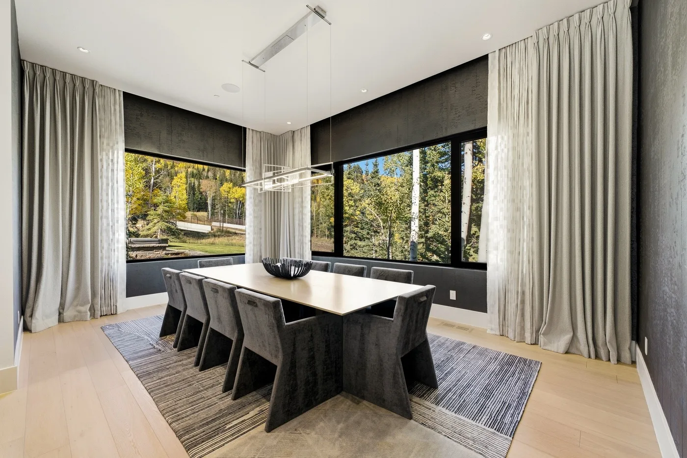 A modern dining area with a large table beside floor-to-ceiling windows.