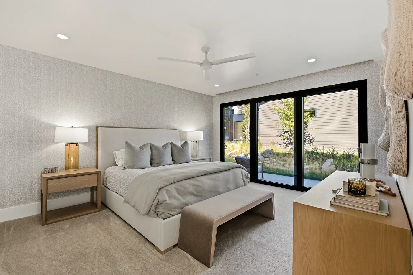 A bright bedroom with a large bed and sliding glass doors opening to a garden view.