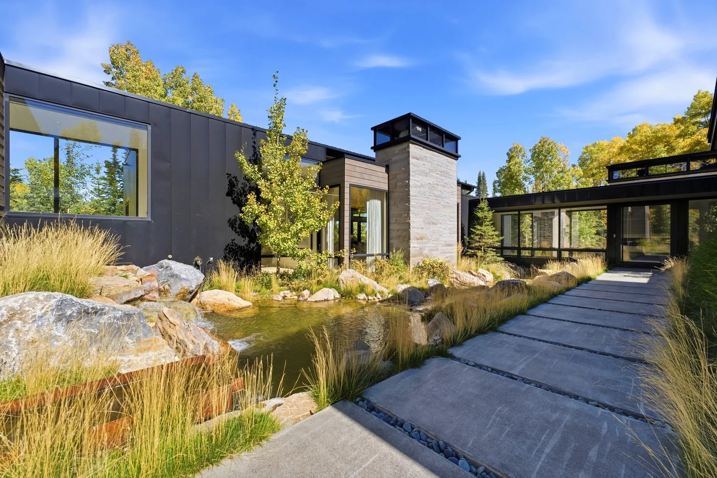 Modern house exterior with a paved path beside a landscaped pond.