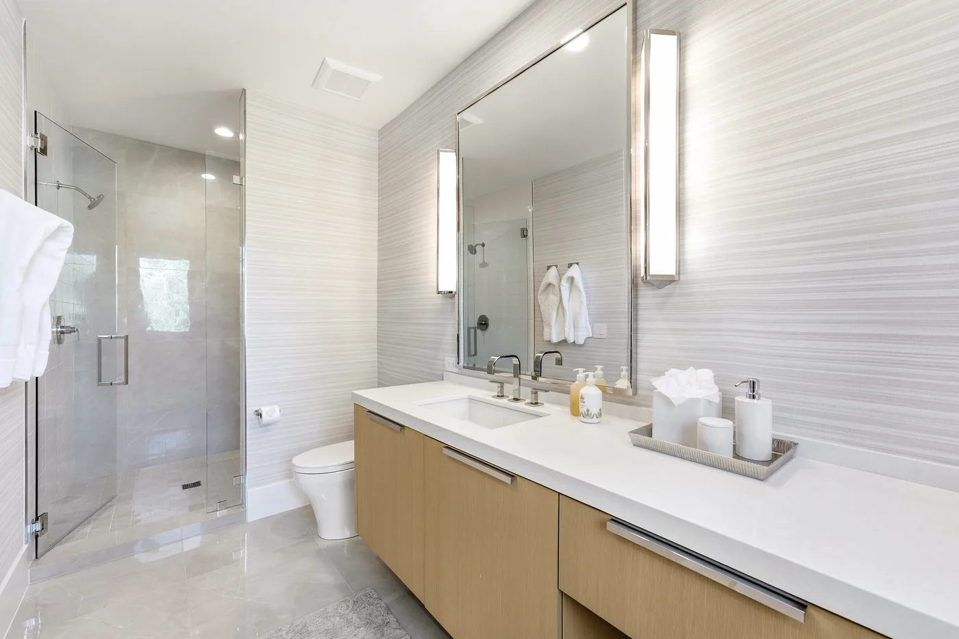A bright bathroom with a glass shower and a long vanity.