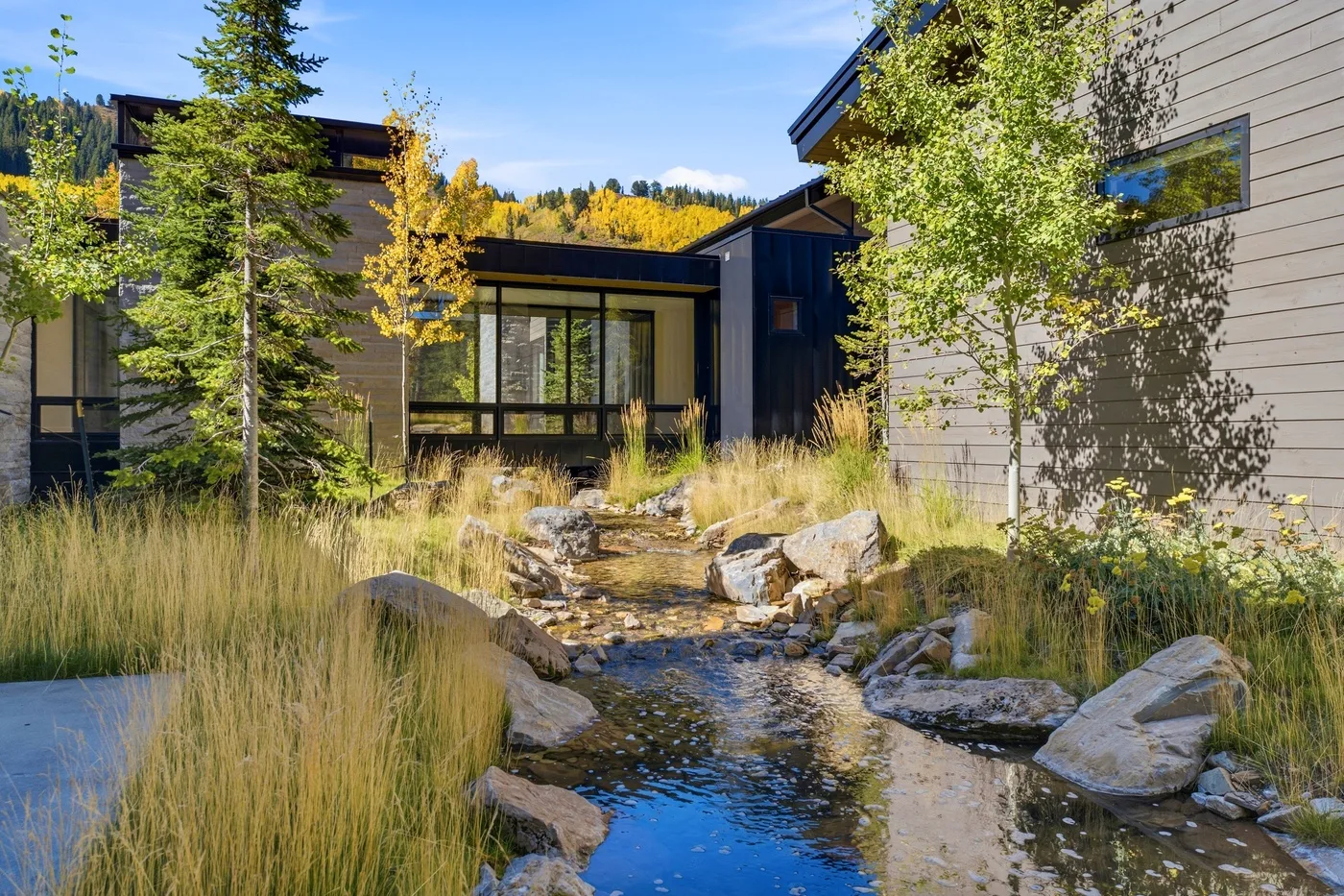 A modern building overlooks a landscaped stream bordered by grasses and rocks.