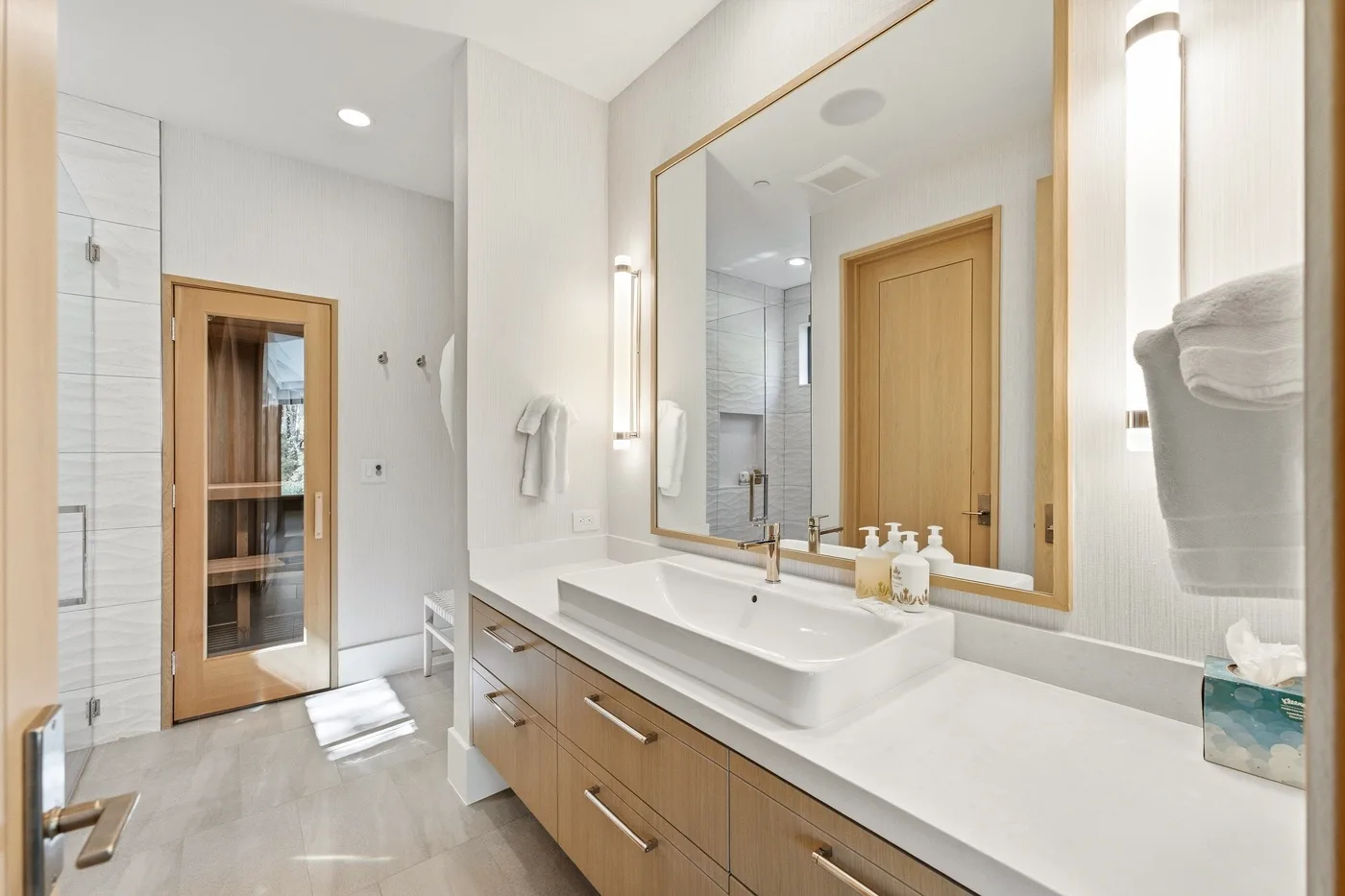A bright bathroom with a wide vanity, a large mirror, and a glass-paneled door.