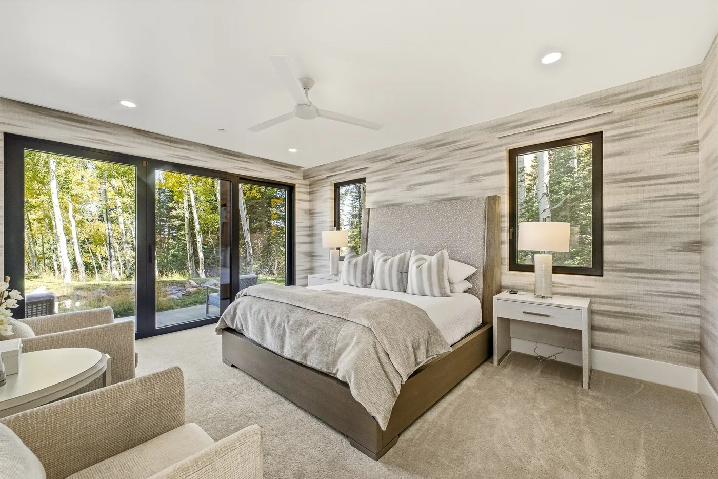 A bedroom with a large bed, bedside tables, and windows overlooking trees.
