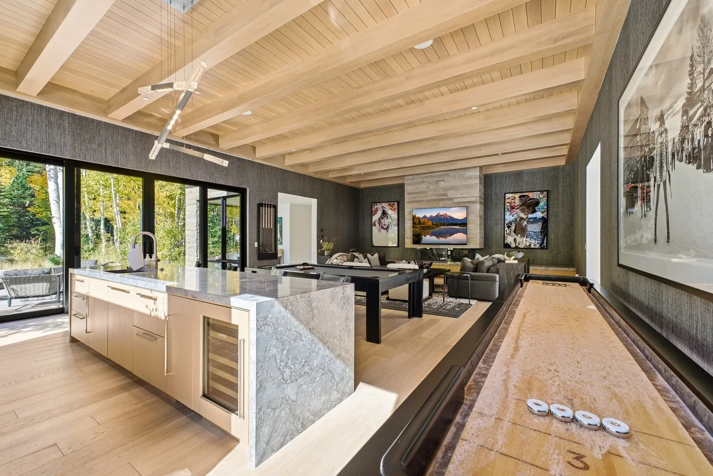 An open kitchen and dining area features a long table beneath a wood-paneled ceiling.