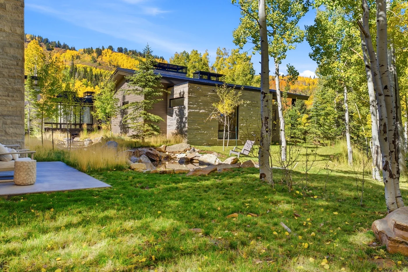 A modern house sits among trees and landscaped grounds beneath a clear blue sky.
