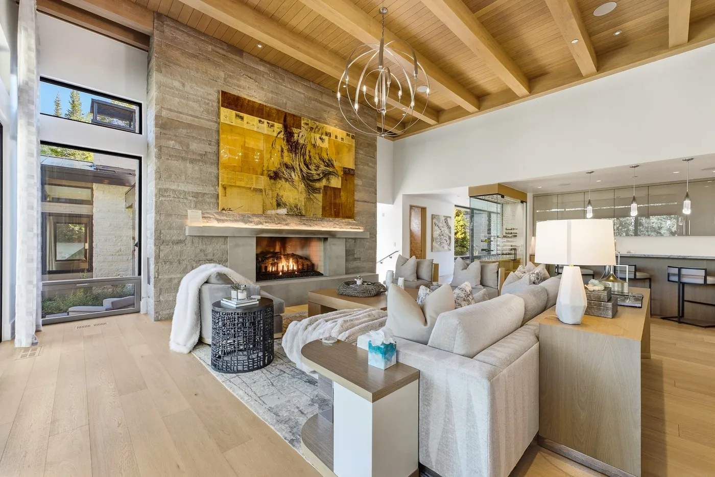 A bright living room with a fireplace, seating, and a dining area beneath a wood-beamed ceiling.