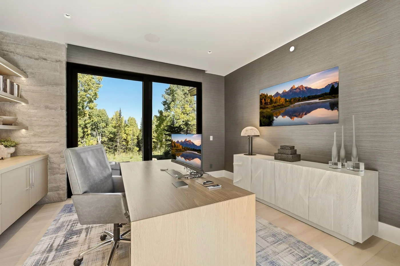 A modern office with a desk, seating, and large windows overlooking trees.