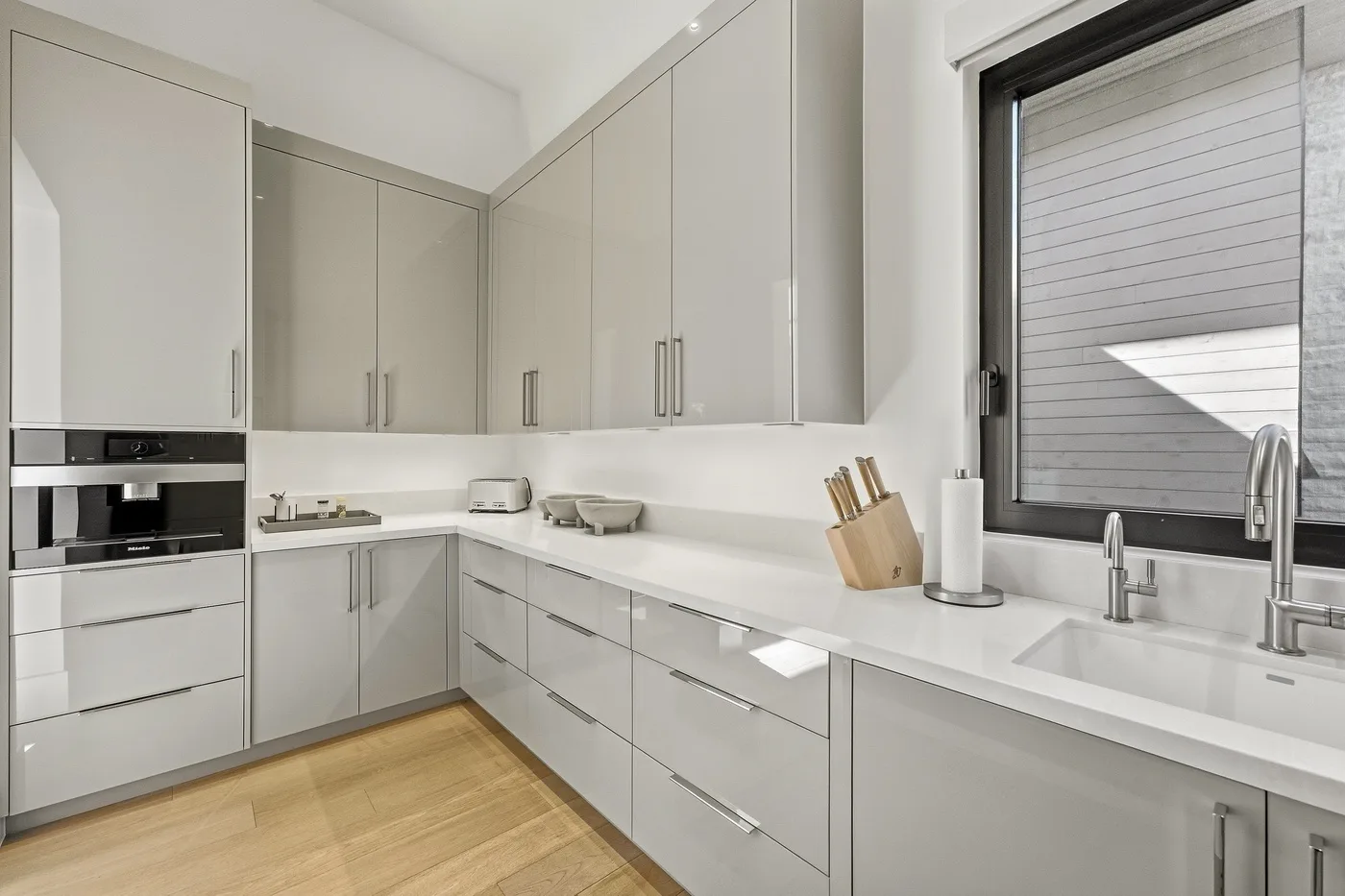 A modern kitchen with gray cabinetry, white countertops, and a large window.