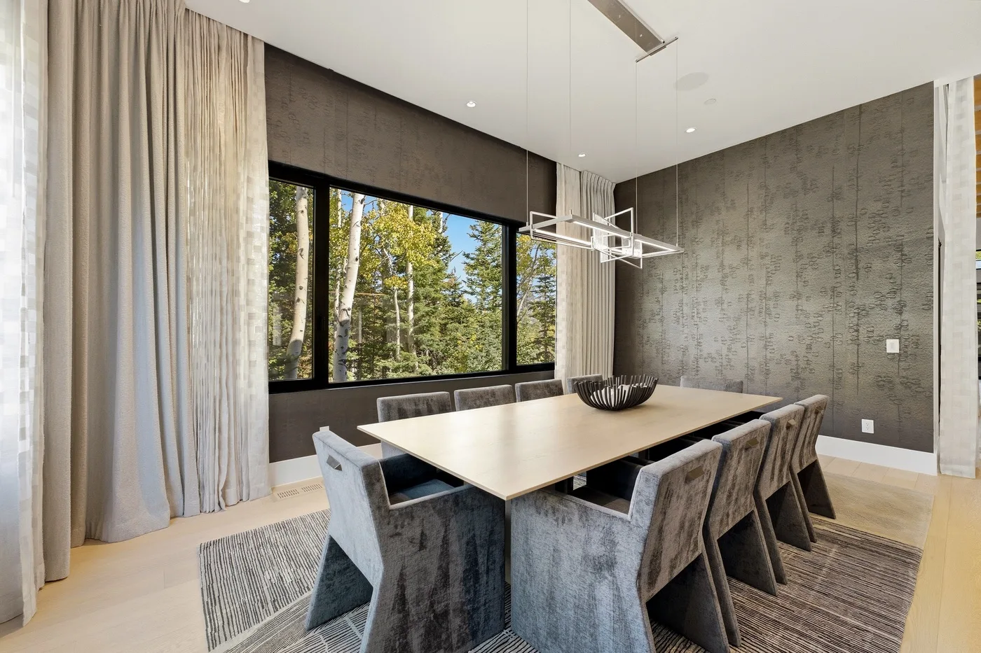 A modern dining room with a large table beside broad windows.