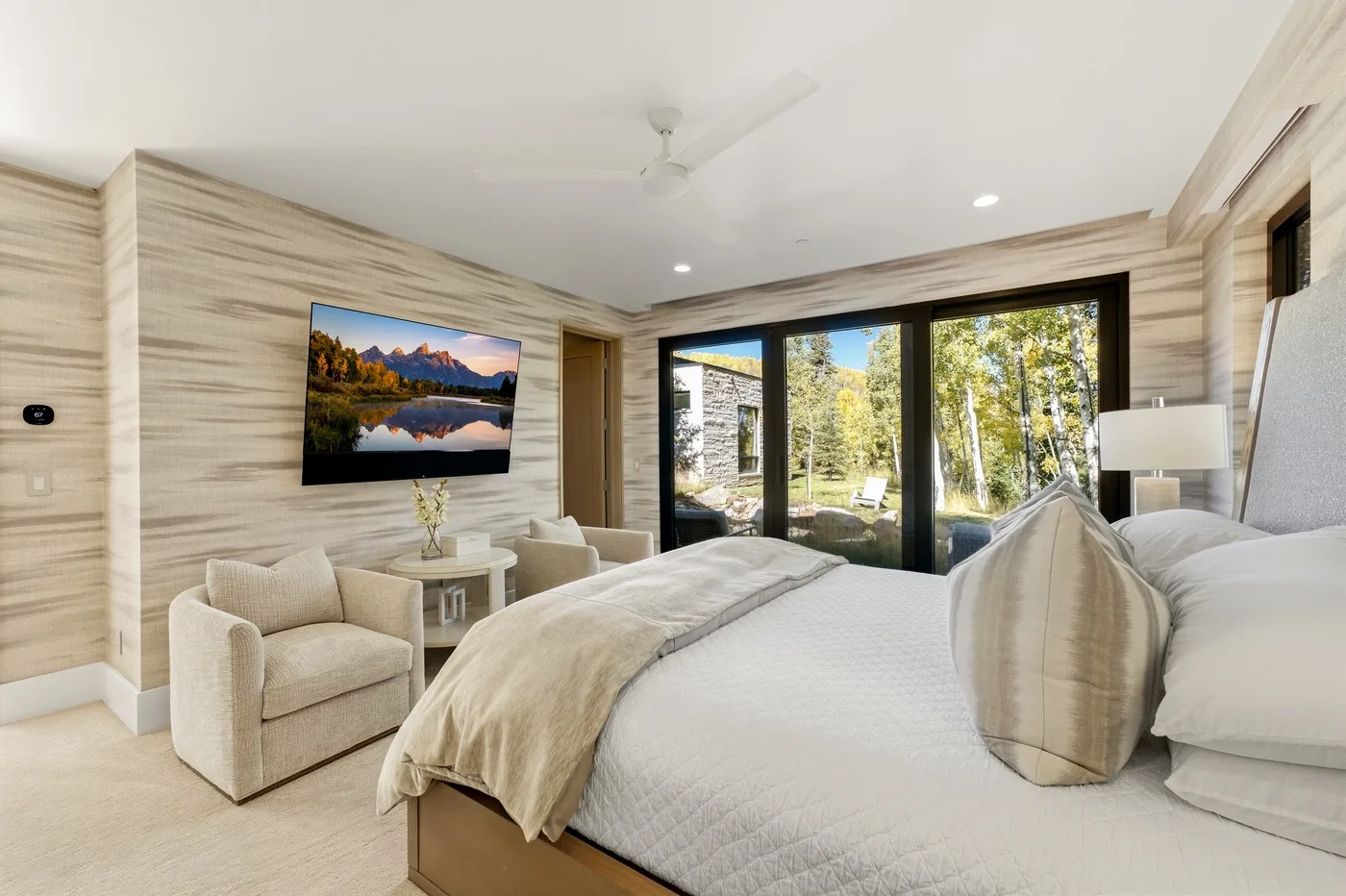 A bright bedroom with a bed, seating, and glass doors overlooking trees.