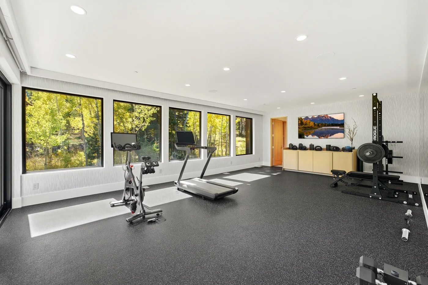 A bright gym with exercise equipment beside large windows.