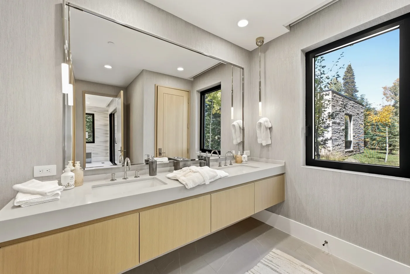 A bright bathroom vanity with a wide mirror and a large window overlooking trees.