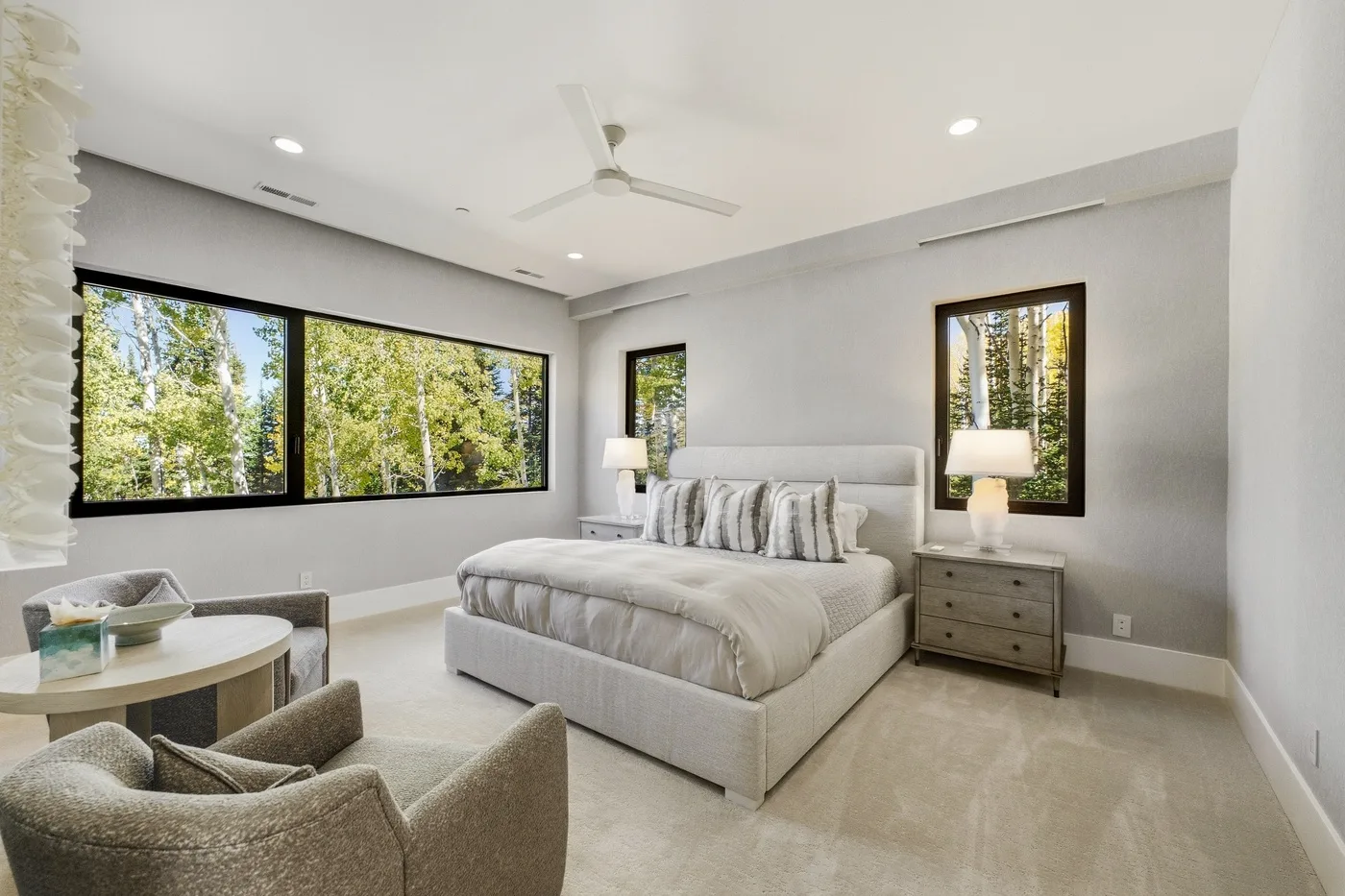 A bright bedroom with a large bed and windows overlooking trees.