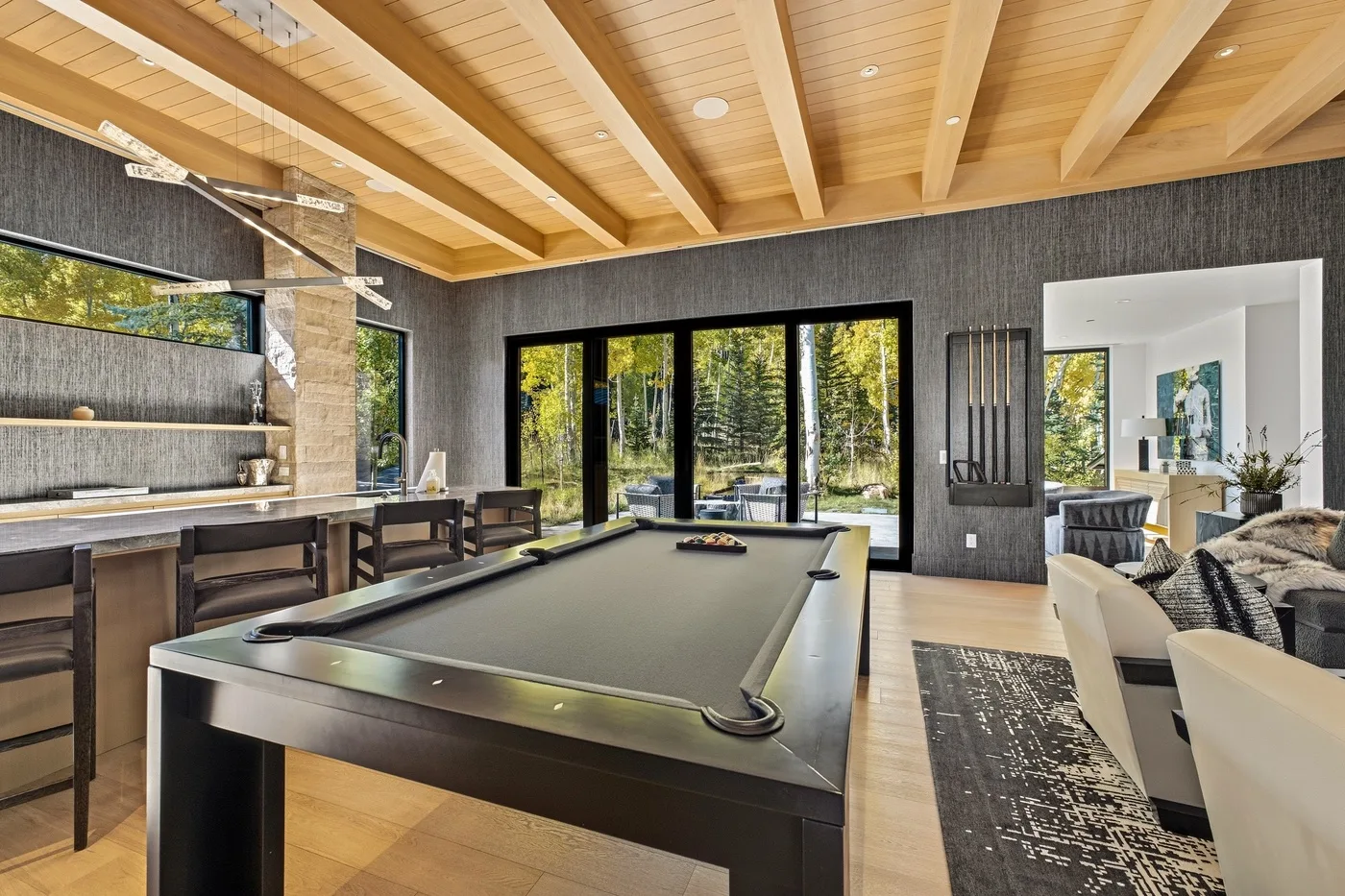 A game room with a pool table, dark walls, and large windows overlooking trees.