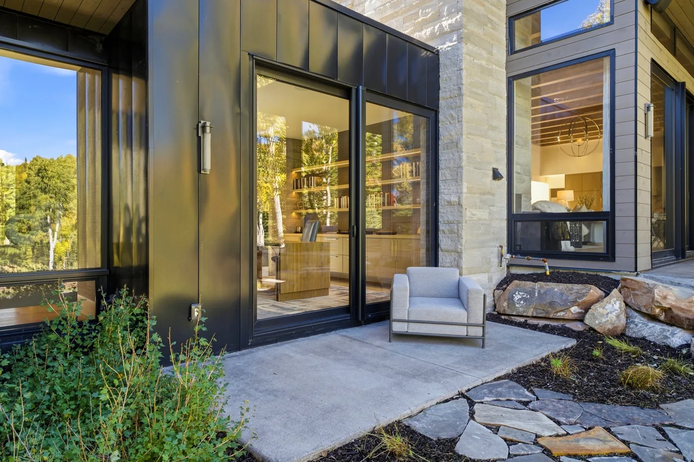 A modern house exterior with large windows, a glass door, and a patio seating area.