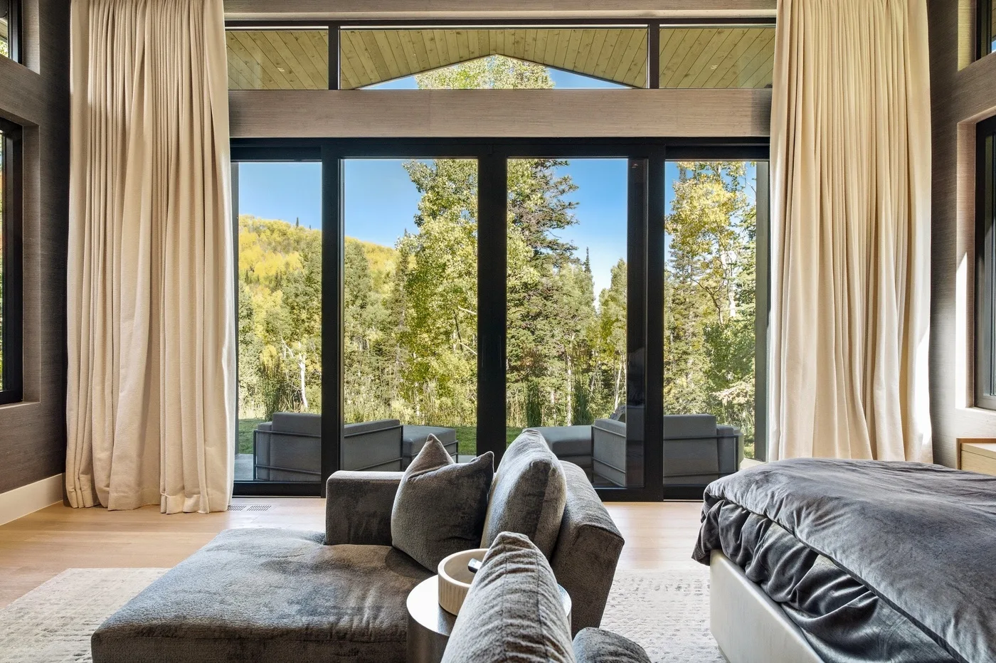 A bedroom with a large glass door opening onto a wooded view.